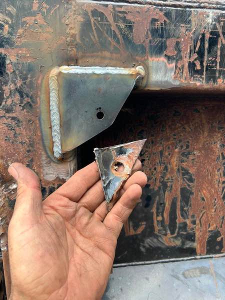 New welded steel bracket on a dump truck next to the broken piece it replaced