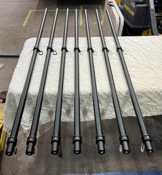 Seven black flag poles laid out on a table in the shop