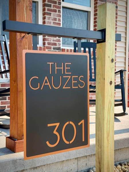 Custom 2 layer plasma cut address sign in black and copper hanging from a custom bracket on a wood post