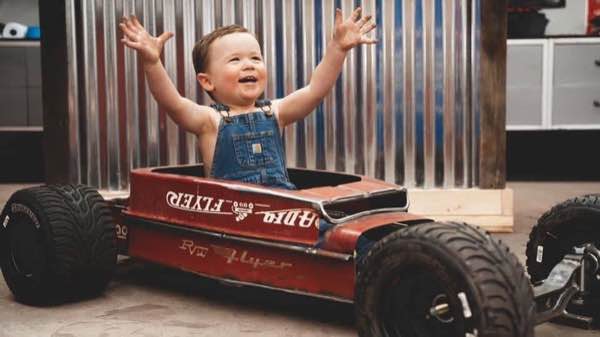 Toddler in overalls with arms up, sitting in a custom hot rod Radio Flyer wagon