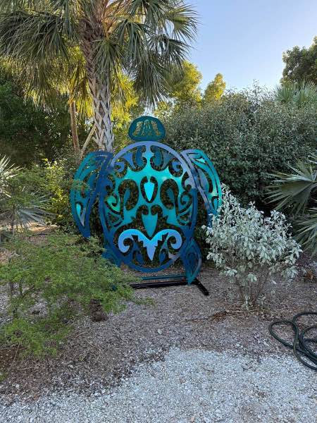 Seven and a half foot tall tribal turtle yard sculpture powder coated in blues and teal, standing in a Florida yard