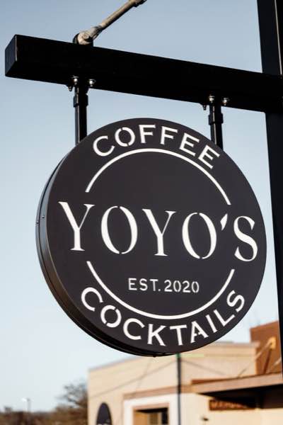 Round black light box style sign for YoYo's Coffee hanging from a steel post